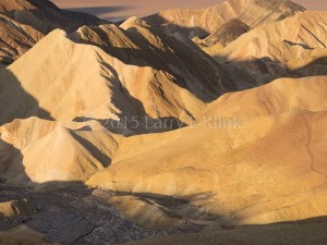 A sculptural landscape of muted earth tones with water standing in both the erosion channels and in the valley below. Zabriske Point, Death Valley, CA OCT 2015. 